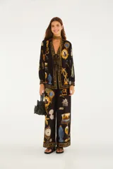 Pantalón largo de silueta amplia, color negro, con diseño estampado de diversos objetos como relojes, palmeras, animales y marcos estilo barroco. Cuenta con cintura elastizada y detalles decorativos en los bordes de la cintura y los tobillos.