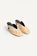 Zapato de tacón destalonado estilo mule, totalmente revestido de abalorios y lentejuelas en tonos claros, con escote en pico, punta cuadrada y tacón medio metalizado.