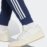 Pantalón de jogging azul marino con tres rayas blancas a los costados y logo de Adidas bordado en el muslo.