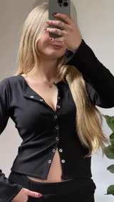 Remera de manga larga en tejido rib negro, con escote redondo y cierre frontal con botones a presión metálicos.