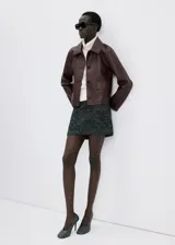 Chaqueta de cuero sintético marrón con cuello camisero, cierre frontal con botones oscuros y bolsillos frontales con solapa.