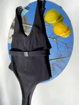 Malla enteriza de punto acanalado color negro, con breteles finos regulables y cinturón con hebilla metálica.