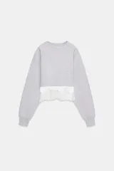 Sudadera crop de cuello redondo y manga larga con puños elásticos. Presenta un diseño de doble capa con un top interior satinado y un bajo decorado con encaje a tono.