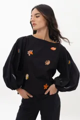 Blusa blanca de algodón con mangas largas voluminosas y escote a la base. Presenta bordados artesanales coloridos con motivos marinos distribuidos en el frente y en las mangas.