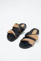 Sandalias planas con base negra y dos tiras anchas superiores, una color beige y otra negra, con efecto arrugado.
