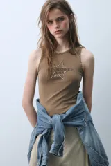 Musculosa de algodón con cuello redondo y diseño sin mangas. Presenta un estampado frontal con el texto Arizona Est. 1975 y detalle de tachas metálicas decorativas en el escote y las sisas.