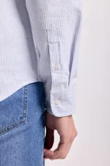 Camisa celeste a rayas verticales blancas, de corte clásico, con cuello abotonado, manga larga y bolsillo en el pecho.