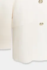 Blazer color blanco roto, de corte cruzado, con cuello solapa, hombreras y manga larga. Presenta falsos bolsillos con solapa en el delantero y cierre frontal con botones metálicos dorados. Confeccionada en hilatura con lino y forro interior a tono.