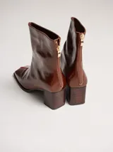 Botas de caña media color marrón, confeccionadas en cuero con acabado brillante. Presentan punta cuadrada, taco de madera y un distintivo bordado decorativo en color rojo que recorre el empeine hasta la punta.