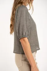 Blusa de algodón con estampado de cuadros vichy en tonos negro y blanco. Presenta escote en V, cierre frontal con botones y mangas cortas abullonadas con terminación elástica.