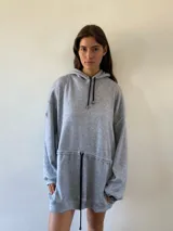 Vestido tipo hoodie oversize de color gris melange, con capucha, cordones ajustables en el cuello y en la cintura, y bolsillos laterales.