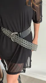 Cinturón ancho de cuero ecológico negro con doble hilera de ojales metálicos plateados y hebilla metálica plateada de estilo occidental.