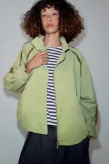 Cazadora ZARA Woman Collection color verde militar, con cuello alto, manga larga y bolsillos frontales. Cuenta con detalles de vivos a contraste en los hombros, bajo elástico asimétrico y cierre frontal oculto con cremallera y botones.
