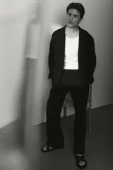 Pantalón negro de tejido suave con corte relajado, cintura elástica con cordón oculto y pliegues frontales. Presenta bolsillos laterales y bolsillos traseros ribeteados.