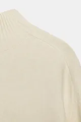 Jersey de punto liso color beige, con cuello subido y manga larga. Presenta acabados en rib en cuello, puños y ruedo.