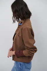 Chaqueta corta color marrón de corte recto, con cuello redondo, cierre frontal de botones y bolsillos frontales tipo parche.