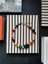 Collar corto de cuentas artesanales multicolores, con piedras y abalorios de diferentes formas, tamaños y texturas, y cadena de ajuste metálica.