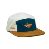 Gorra de cinco paneles con diseño color block que combina paneles laterales en color crema, panel frontal en azul petróleo y visera plana en color marrón. Presenta un bordado central con forma de diamante y un detalle bordado lateral con el nombre de la marca.