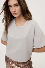 Remera gris de fit amplio, con mangas cortas y cuello redondo. Presenta efecto lavado y estampa frontal con aplicación de strass con la frase "fiesta mode on".
