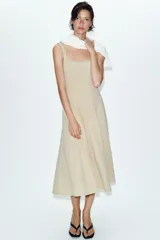 Vestido midi de color beige con escote cuadrado y tirantes anchos. Presenta un diseño entallado en el torso con costuras verticales marcadas y una falda con caída evasé.