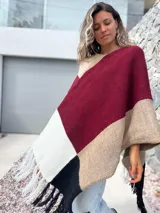 Poncho tejido de punto con diseño de bloques de color en tonos bordó, beige, blanco y negro, con terminación de flecos en el ruedo.