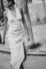 Vestido midi de lino con cuello halter y escote en pico. Presenta un diseño con frunces en el delantero, abertura lateral y cierre posterior con cremallera oculta y botones.
