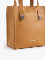 Cartera tipo tote pequeña de cuero color tostado, con doble asa superior y herrajes metálicos plateados en forma de llama en la base de las manijas. Presenta el logo de la marca estampado en la parte inferior frontal.