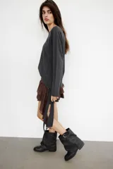 Falda pantalón de tiro bajo en color negro, con cintura drapeada y detalle de tira lateral colgante. Presenta un diseño con volantes en el bajo y cierre de cremallera metálica.