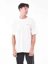 Remera blanca de corte oversize con cuello redondo y manga corta. Presenta un pequeño texto bordado en el pecho que dice "what now?".