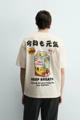 Camiseta relaxed fit color crema, con cuello redondo y manga corta. Presenta un estampado frontal con caracteres japoneses en negro y contorno rojo.