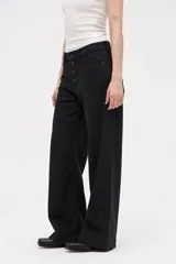 Jean de corte wide leg en color negro, con tiro medio y cierre frontal con botones a la vista. Presenta un diseño holgado desde la cadera hasta el bajo, con pierna ancha.