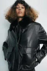 Chaqueta de efecto piel en color negro, con cuello de solapa con aplicación de pelo sintético, manga larga y bolsillos frontales de plastrón con solapa. Cierre frontal con cremallera y botones ocultos bajo solapa.