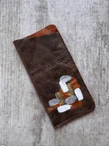 Portalentes de cuero marrón chocolate con arte pintado a mano en tonos cobre, dorado y blanco, y logo grabado de la marca Carolina de Cunto.