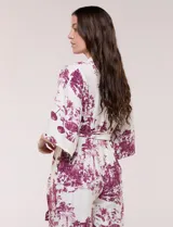 Enterito largo de calce fluido con escote en V cruzado, mangas 3/4 anchas, cintura elastizada con lazo ajustable y pantalón wide leg con bolsillos laterales. Estampado tipo toile de Jouy en tonos violeta sobre fondo blanco.