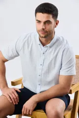 Camisa de manga corta confeccionada en mezcla de lino y algodón, con diseño de rayas verticales en tonos celeste y blanco. Cuenta con cuello camisero, botonadura frontal y bordado sutil en el pecho.