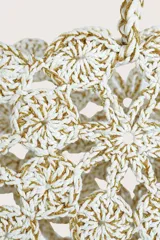 Bolso tipo cesta tejido a crochet con diseño de flores caladas en color blanco y detalles dorados. Cuenta con asas trenzadas y una etiqueta decorativa de cuero sintético marrón.