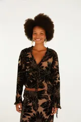 Blusa de manga larga con escote en V, cierre frontal con lazos ajustables y terminaciones de volados en cuello y puños. Confeccionada en tejido semitransparente con diseño floral aterciopelado.