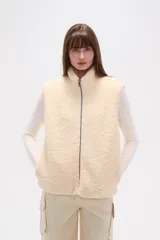 Chaleco sin mangas de textura peluche (teddy) color crema, con cuello alto y cierre frontal de cremallera.
