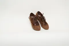 Zapatillas de cuero gamuzado color marrón pecán, con recortes laterales que aportan ventilación, detalles metalizados en tono bronce y cordones al tono. Cuenta con suela baja de goma.