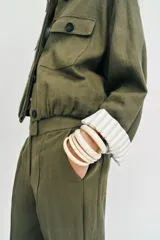 Chaqueta corta de color verde militar, con cuello solapa, bolsillos delanteros con solapa y cierre frontal de botones ocultos. Presenta mangas amplias con vuelta en los puños que muestran un forro a rayas.