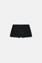 Bermudas de tiro medio y cintura ancha, color marrón, con bolsillos delanteros y cierre frontal con cremallera y ganchos metálicos.