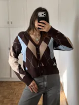 Saco tejido de punto con estampado de rombos en tonos marrón, celeste y beige, con escote en V, manga larga y cierre frontal con botones oscuros.