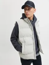 Chaleco puffer acolchado de color gris claro, con cuello alto y cierre frontal con cremallera. Cuenta con bolsillos laterales y diseño versátil sin mangas.