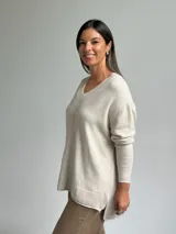 Sweater de punto color beige con escote en V, diseño holgado y costura central vertical. Presenta mangas largas con puños acanalados y ruedo con terminación acanalada.