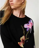 Sweater negro de algodón con cuello redondo, manga larga y corte holgado. Presenta incrustaciones florales decoradas con bordados a mano.