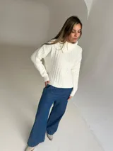 Jersey de punto color crudo con cuello alto y diseño acanalado vertical. Presenta un corte holgado y mangas largas con puños ajustados.