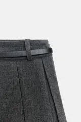 Falda pantalón de tiro alto con diseño de tablas, confeccionada en tejido gris. Incluye un cinturón fino de cuero sintético con hebilla metálica dorada y cierre lateral con cremallera oculta.