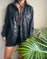 Camisa negra de cuero sintético con botones dorados, bolsillos frontales y corte holgado.