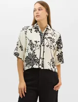 Camisa de corte holgado con estampado botánico en blanco y negro. Presenta cuello camisero, mangas cortas amplias y cierre frontal con botones y vivos a contratono.