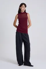 Top sin mangas color negro, con cuello alto y tejido de punto fino y transparente en la parte superior del pecho y espalda, y tejido opaco en la parte inferior.